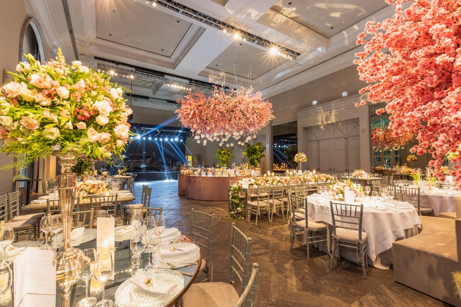 An elegantly decorated indoor wedding reception setup at Morden Hall Park, featuring a floral arrangement with a large, lush bouquet of pale pink roses, white lisianthus, and greenery in a tall silver