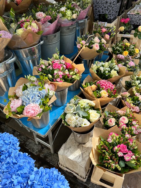 An array of fresh flower bouquets arranged in metal and brown paper wrapping on a display table at a flower shop. The bouquets feature pink, white, and pale green roses, hydrangeas, and other blossoms