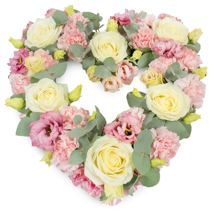The photograph captures a detailed view of a heart-shaped funeral wreath, meticulously composed from pastel flowers and subtle foliage, set before a pristine white backdrop. This clean background makes the blush, cream, and green tones appear especially soft and luminous. At the heart of the design are prominent roses in shades of creamy ivory and pale yellow, their petals tightly spiralled at the centre and unfolding in smooth, rounded layers toward the edges. These roses act as emotional anchors in the wreath, symbolising love and respect. Interwoven between them, clusters of light pink carnations form a dense, textured layer, with each ruffled petal overlapping to create a sense of abundance and gentle movement. Adding depth and variation, deeper pink and mauve lisianthus flowers are scattered throughout the arrangement, their slightly more open, trumpet-like blooms and occasional darker centres lending a quiet intensity, like the deepening sky over Morden as evening draws in. Silvery-green eucalyptus foliage is threaded delicately between the blossoms, its distinctive rounded leaves and muted tones creating a cool, calming contrast to the warmer pastels. Small, tightly furled yellow-green buds punctuate the design, suggesting renewal and continuity. The flowers are positioned closely, so the heart outline is clearly defined and fully padded, with no open gaps, giving the whole piece a luxurious, enveloping quality. The mood conveyed is one of serenity, remembrance, and heartfelt condolence, making this wreath ideal for serving as a focal tribute at a funeral in Morden, a memorial service near Morden Hall Park, or a final gesture of love at a graveside. Carefully arranged, it embodies the sensitive craftsmanship and quiet empathy of Florist Morden, reflecting the community's gentle way of honouring those who have passed.