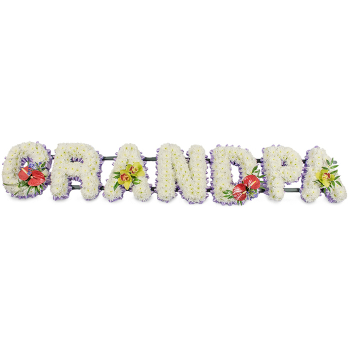 This personalised funeral arrangement presents the word "GRANDPA" in substantial floral lettering, the kind of meaningful tribute often delivered to services and chapels around Morden. Each capital letter is densely covered with fresh white chrysanthemums, their small, rounded blooms layered so tightly they form continuous, cushion-like blocks of texture. The white petals create an impression of softness and stillness, as though the flowers are gently cradling the name of a beloved grandfather. Tiny glimpses of green at the centres of some chrysanthemums add a whisper of natural colour, suggesting freshness and careful conditioning by a skilled local florist. At the base of each letter, a narrow band of pale lavender ribbon provides a delicate contrast, tracing a soft purple line that separates the floral letters from the clean white background. The tribute is supported by sturdy dark green bars running along the back, mostly hidden from view but essential for keeping the design upright and secure during a funeral procession or cremation ceremony. Splashes of colour appear in four thoughtfully placed sprays: on the letters "G" and "D", bold red anthuriums stand out with their glossy, heart-shaped petals and bright yellow spadices, nestled among deep green foliage and perhaps a hint of smaller blooms, symbolising strong, enduring love. On the first and last "A", graceful yellow-green orchids add movement and sophistication, their arching stems and intricate petals lending a contemporary note to the otherwise classic tribute. Overall, the arrangement conveys a quiet, heartfelt message, a bespoke "Grandpa" floral display that would feel perfectly at home in a Morden service, honouring a life with gentleness, beauty and respect.